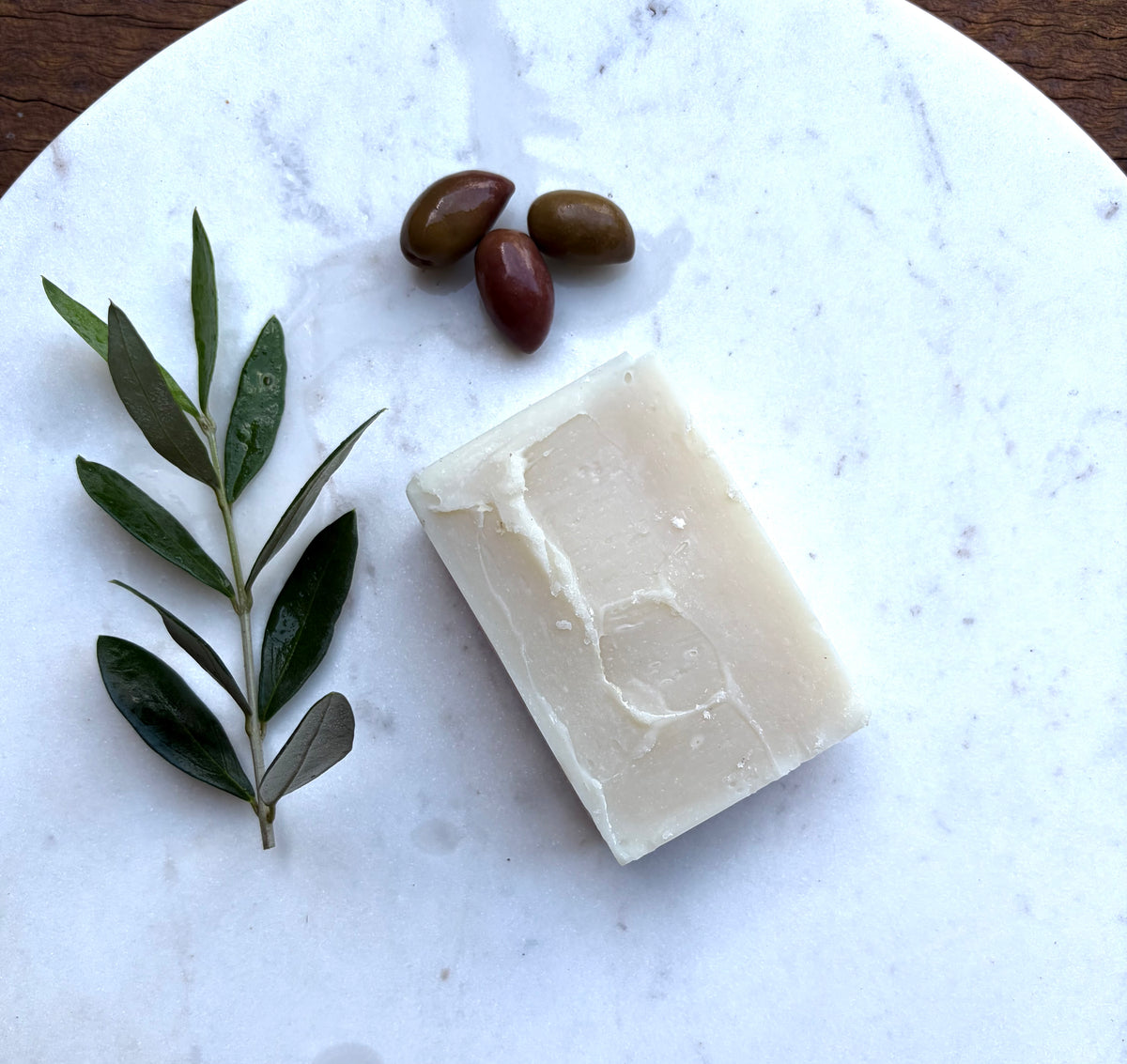 Natural bar of soap with olives and olive branch on marble The Herbal Gardener
