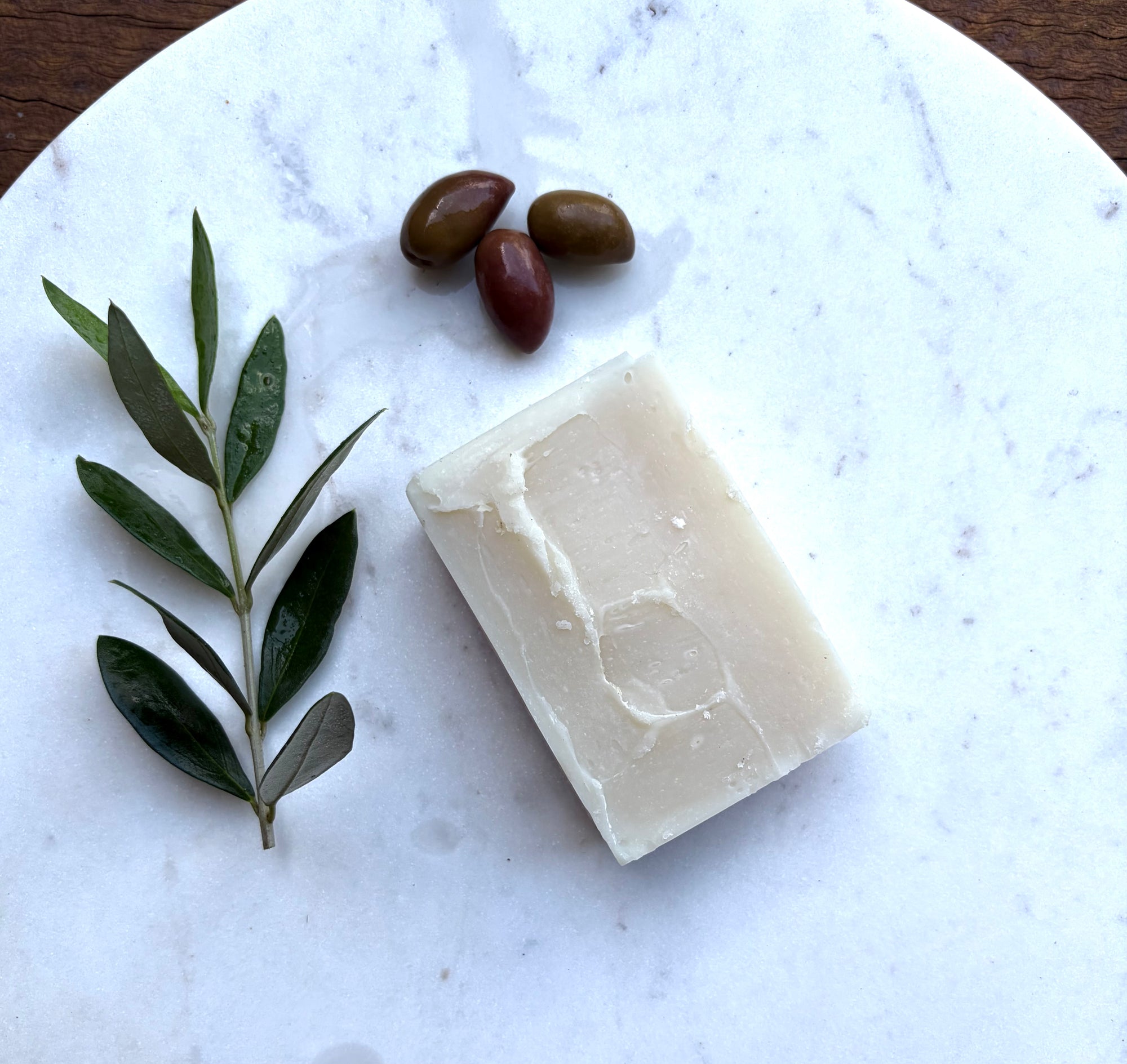 Natural bar of soap with olives and olive branch on marble The Herbal Gardener