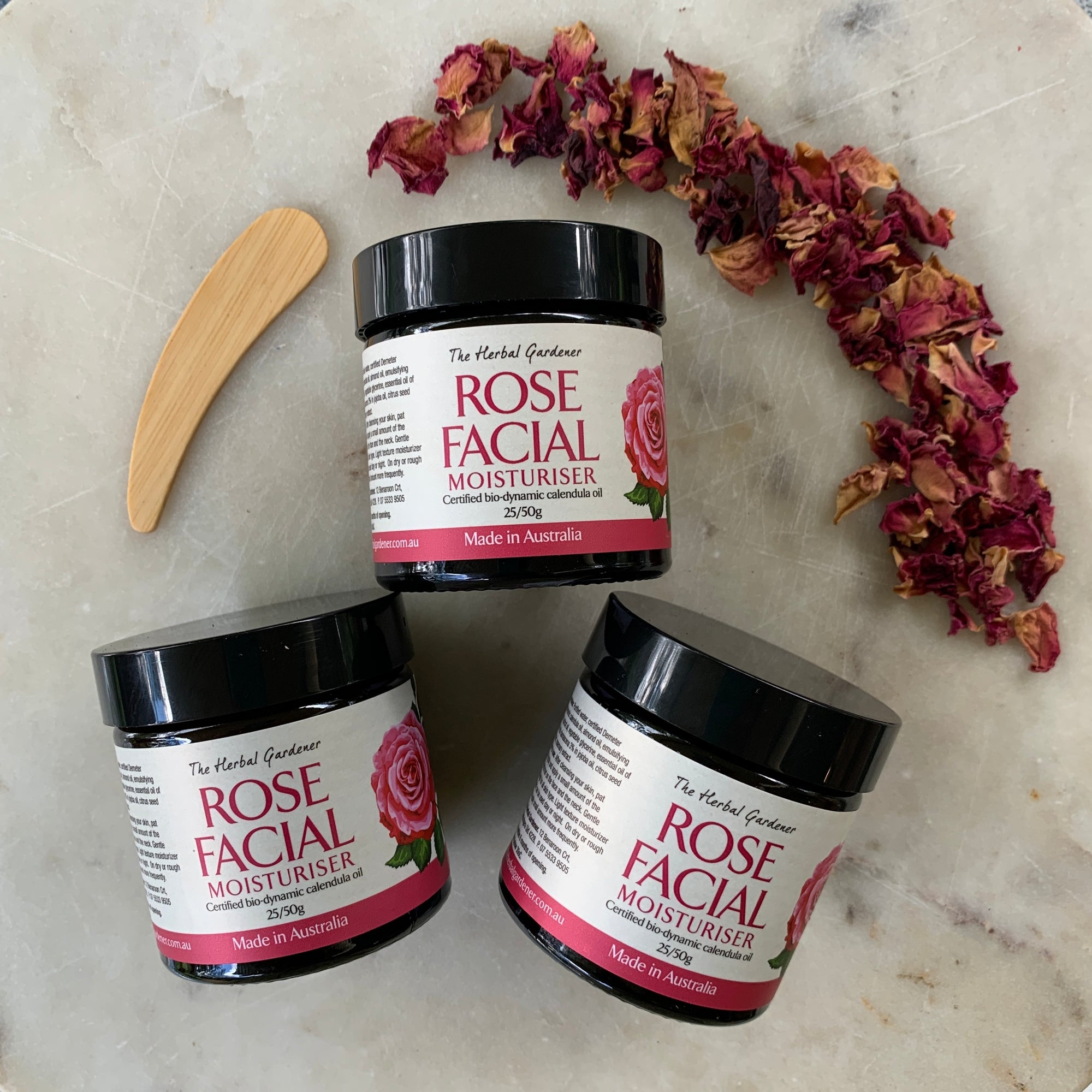 Rose Facial Moisturiser Three Pack 50gr each with a wooden spoon and dried rose petals on a marble surface The Herbal Gardener